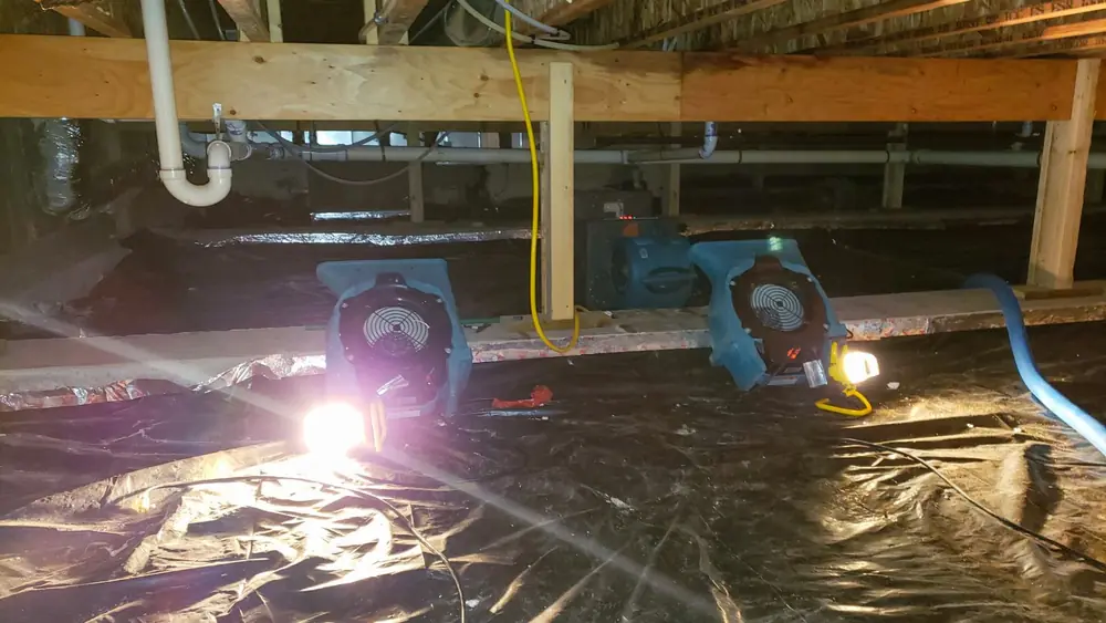 Air movers and a work light running over plastic sheeting in a crawl space