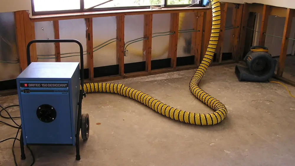 Dehumidifier and air mover with a yellow duct hose in a room where the wall cavities are open