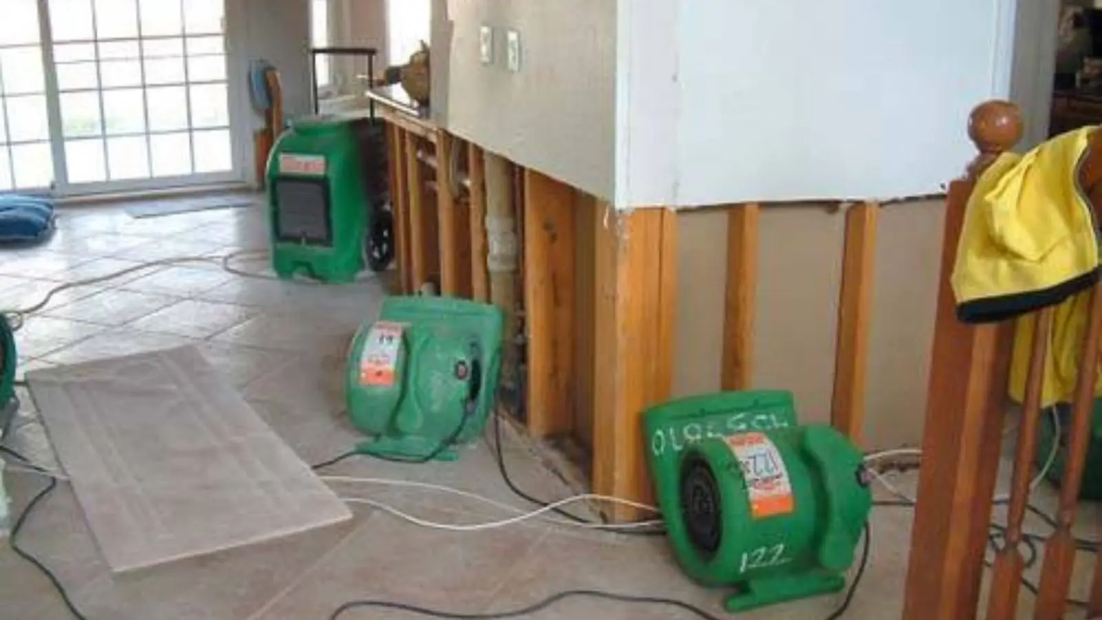 Green air movers and a dehumidifier running in a room with open wall cavities