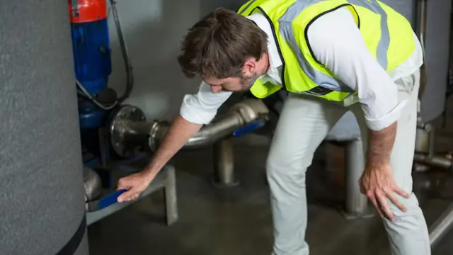 Technician in a high-visibility vest checking a pump and pipe